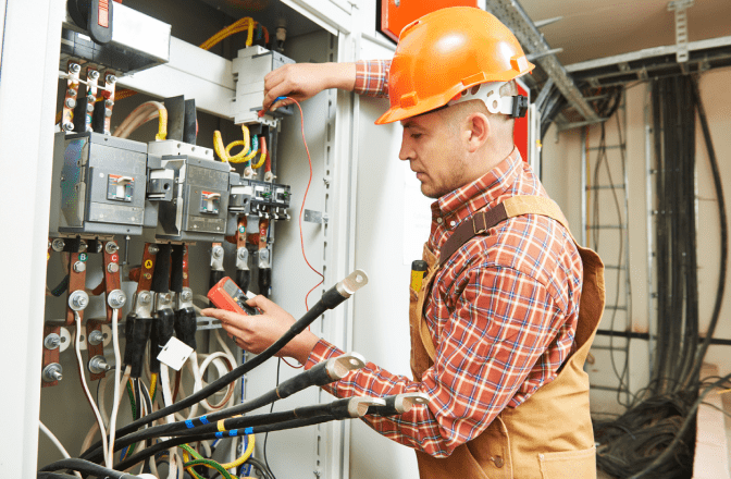 An electrician works on a complex electrical panel, checking connections and components.