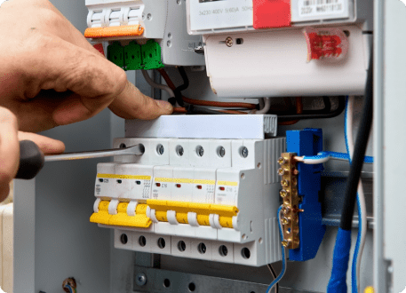 An electrician uses a screwdriver to adjust circuit breakers in an electrical panel.