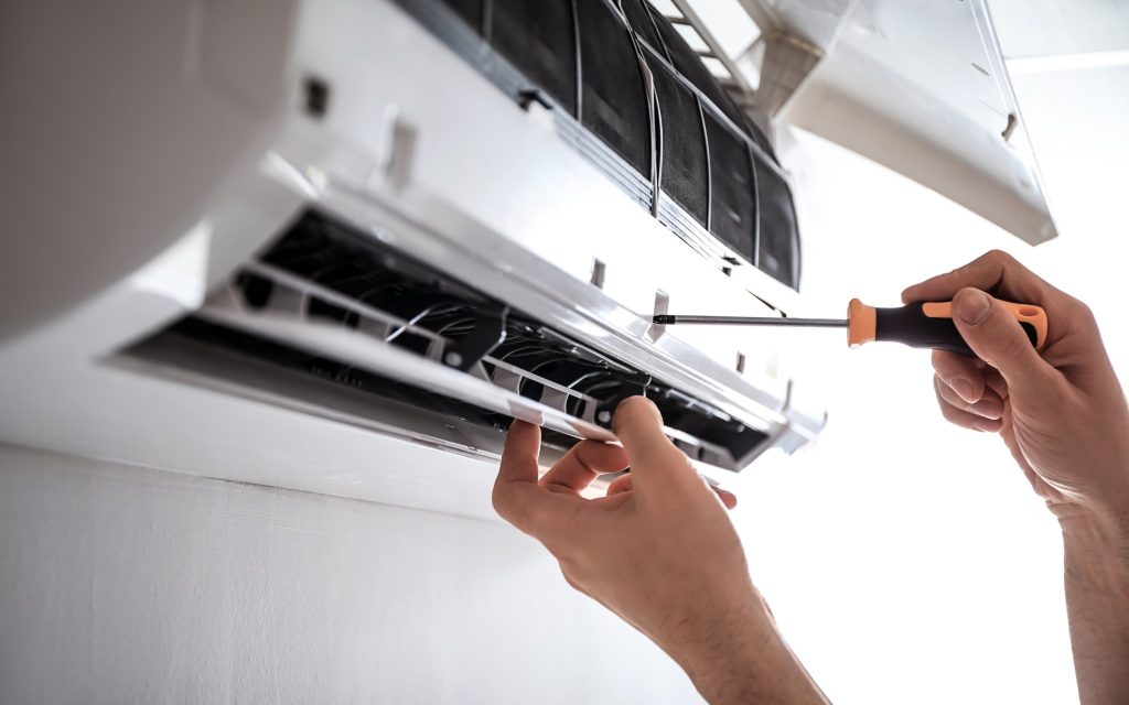 Technician performing air conditioning maintenance with screwdriver on wall-mounted split AC unit, Brisbane and Sunshine Coast aircon service