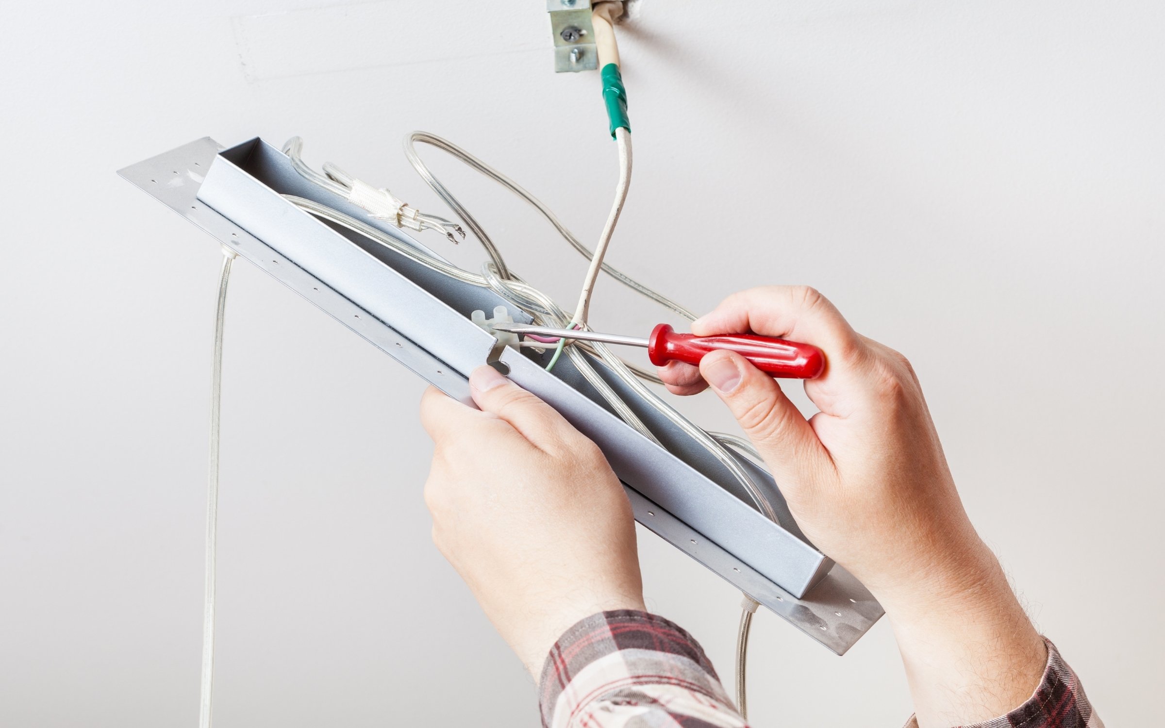 Electrician installing ceiling light fixture wiring using red screwdriver with metal frame