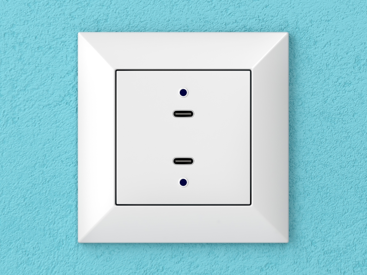 A white wall socket with two USB-C ports, set against a textured light blue wall. This modern, square USB power point features blue indicator lights next to each port for a sleek and functional upgrade to any space.